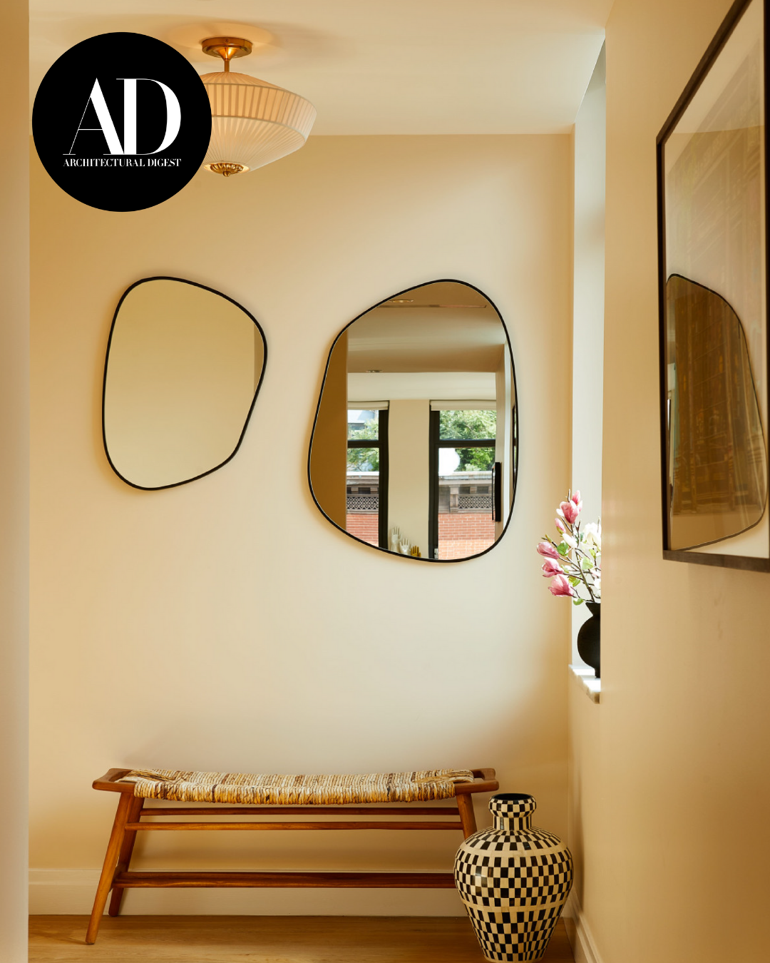 Architectural Digest–featured hallway with sculptural mirrors and a wooden bench.