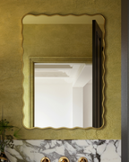 Rectangular wall mirror with a softly wavy gold frame mounted on a textured wall above a marble vanity.