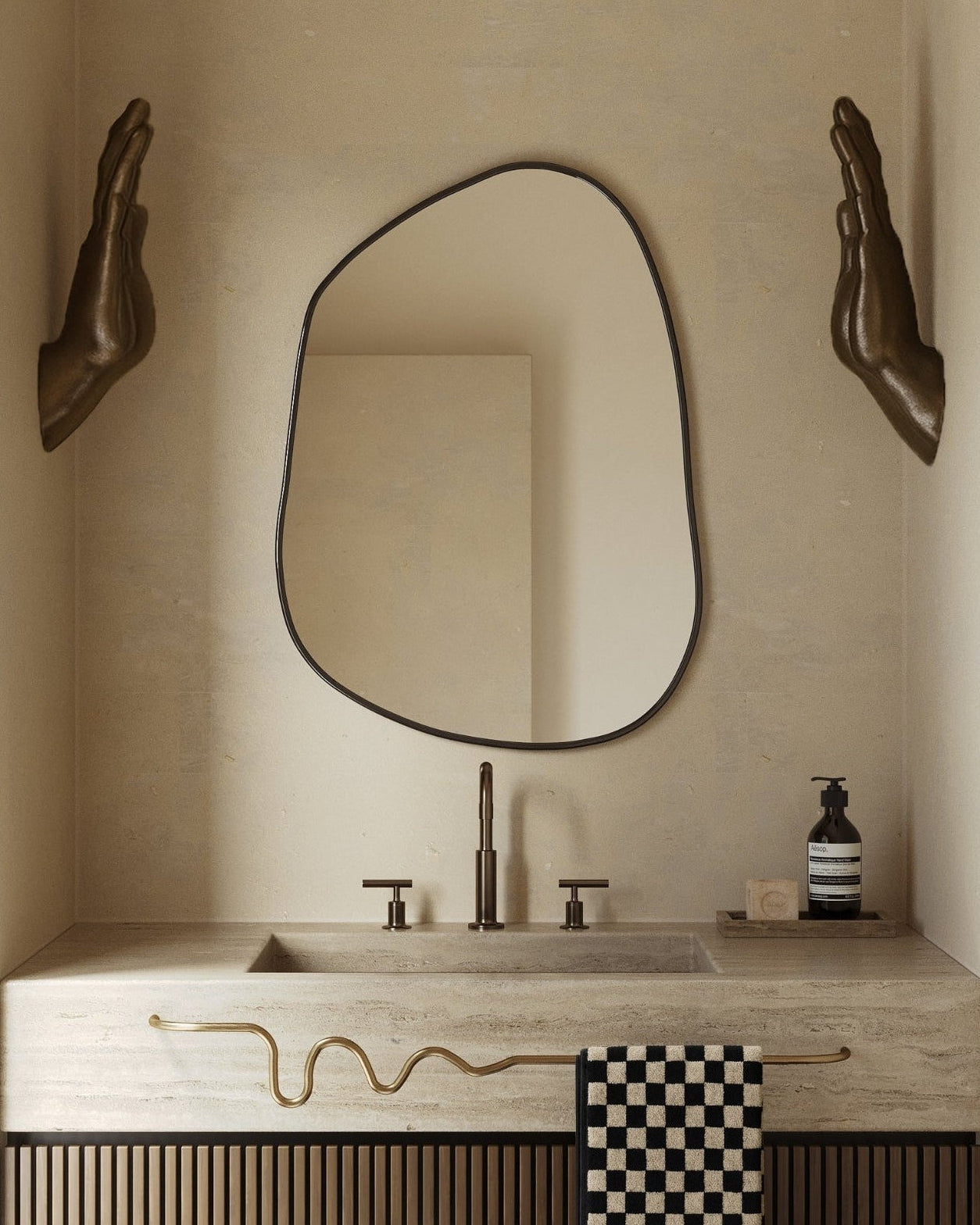 Asymmetrical wall mirror mounted above a stone bathroom vanity with bronze fixtures.