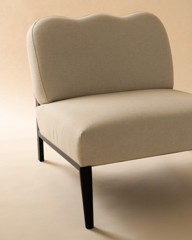 A beige upholstered accent chair with a curved backrest and black legs, set against a neutral background.