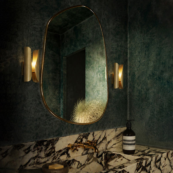 Wall-mounted oval mirror with gold frame in a darkly decorated room.