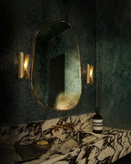 Wall-mounted oval mirror with gold frame in a darkly decorated room.