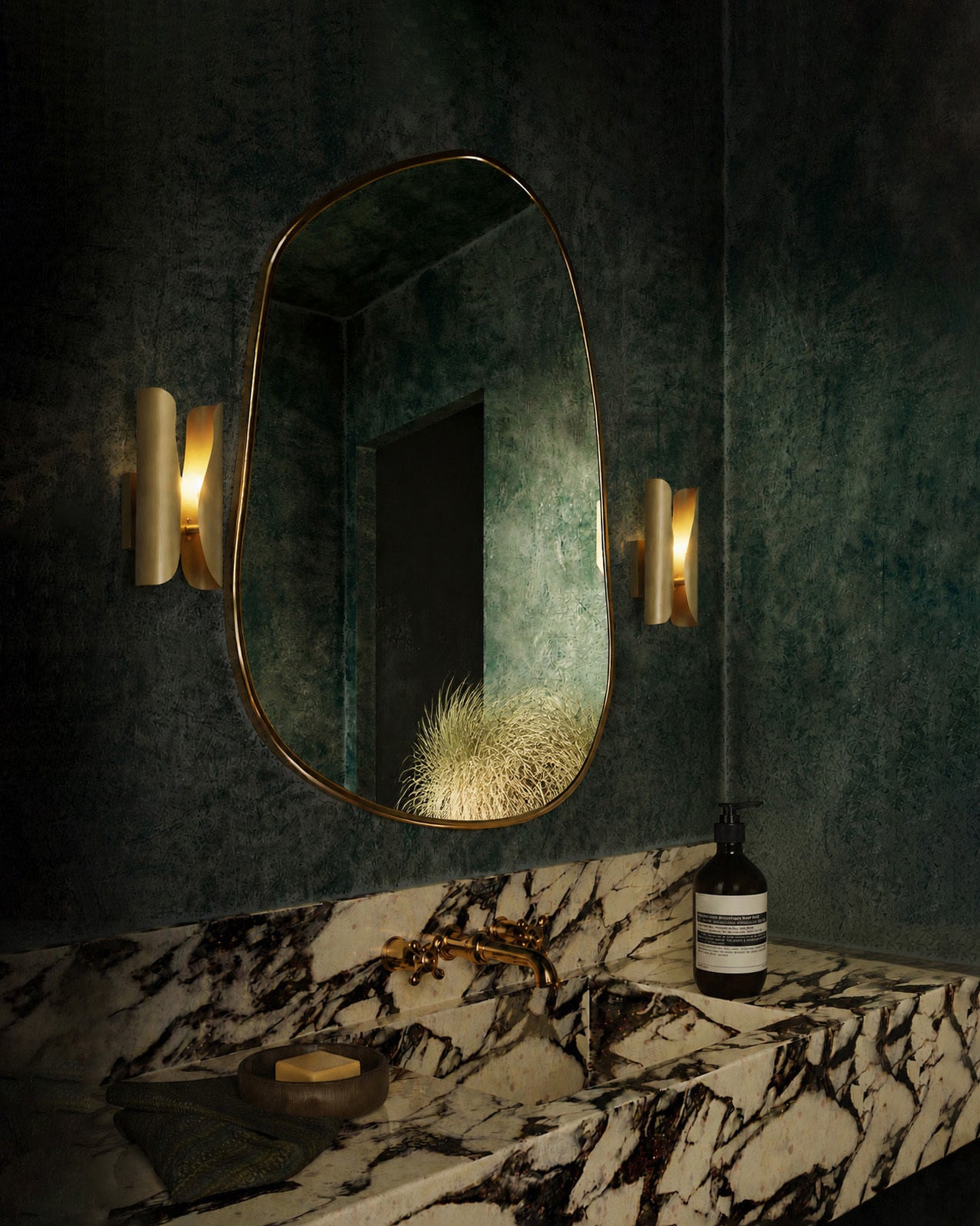 Wall-mounted oval mirror with gold frame in a darkly decorated room.