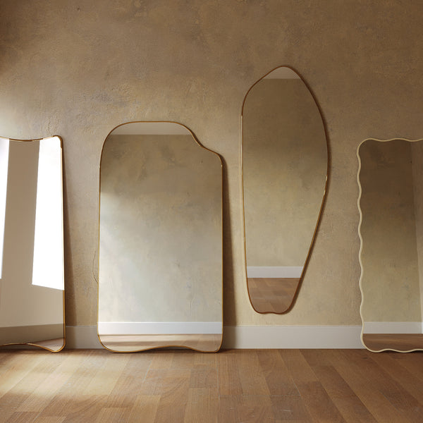 Collection of organic-shaped mirrors with brass frames leaning against a wall.