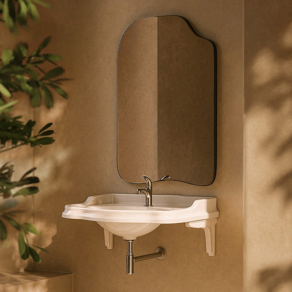 Asymmetrical wall-mounted mirror with a thin black frame above a wall-mounted sink in a bathroom setting.
