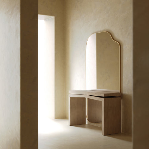 An organic-shaped full length mirror mounted above a minimalist wooden console table in a softly lit, neutral-toned interior.