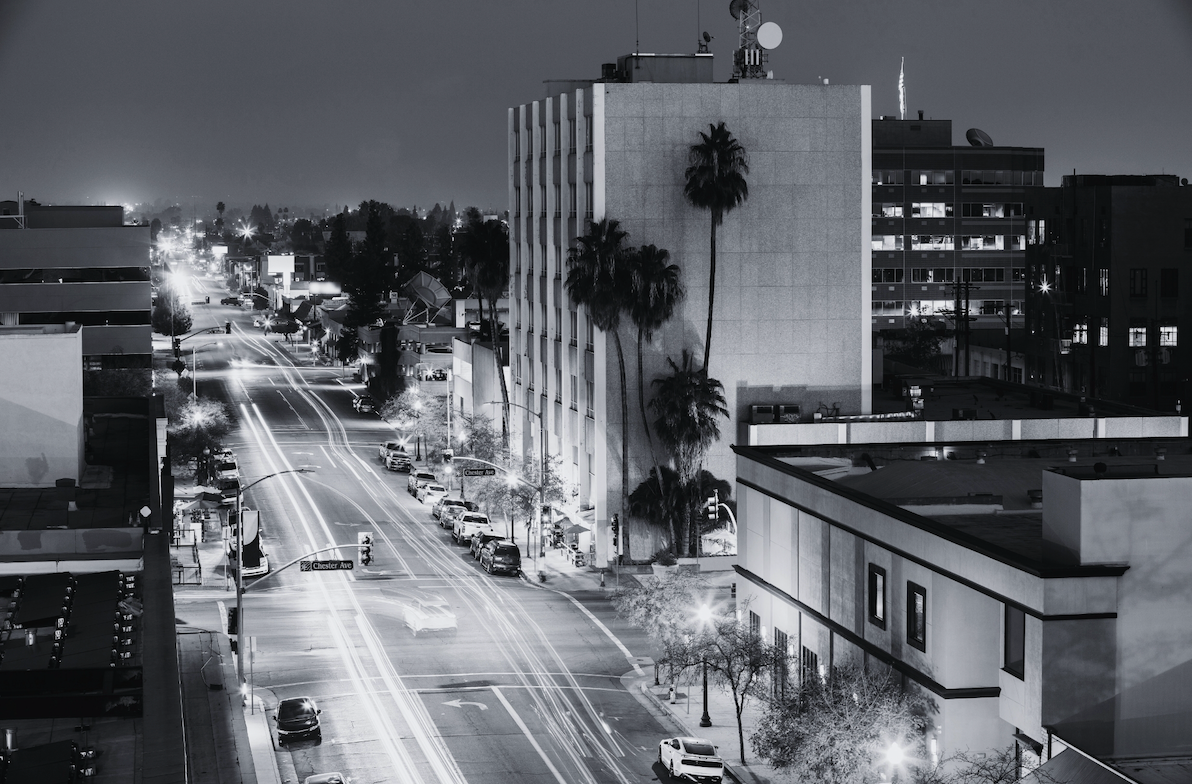 Nighttime city street in California with palm trees and light trails from traffic.