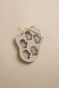A beige, mitten-shaped silicone mold with five mitten cavities, tied with a small bow, shown with frozen shapes inside on a neutral background.
