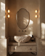 Clove Mirror with decorative beaded edge mounted above a carved stone sink and wall sconces.