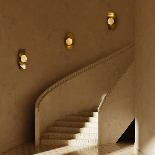 Three oval wall sconces with gold finishes and round white globes mounted along a curved stairwell wall.