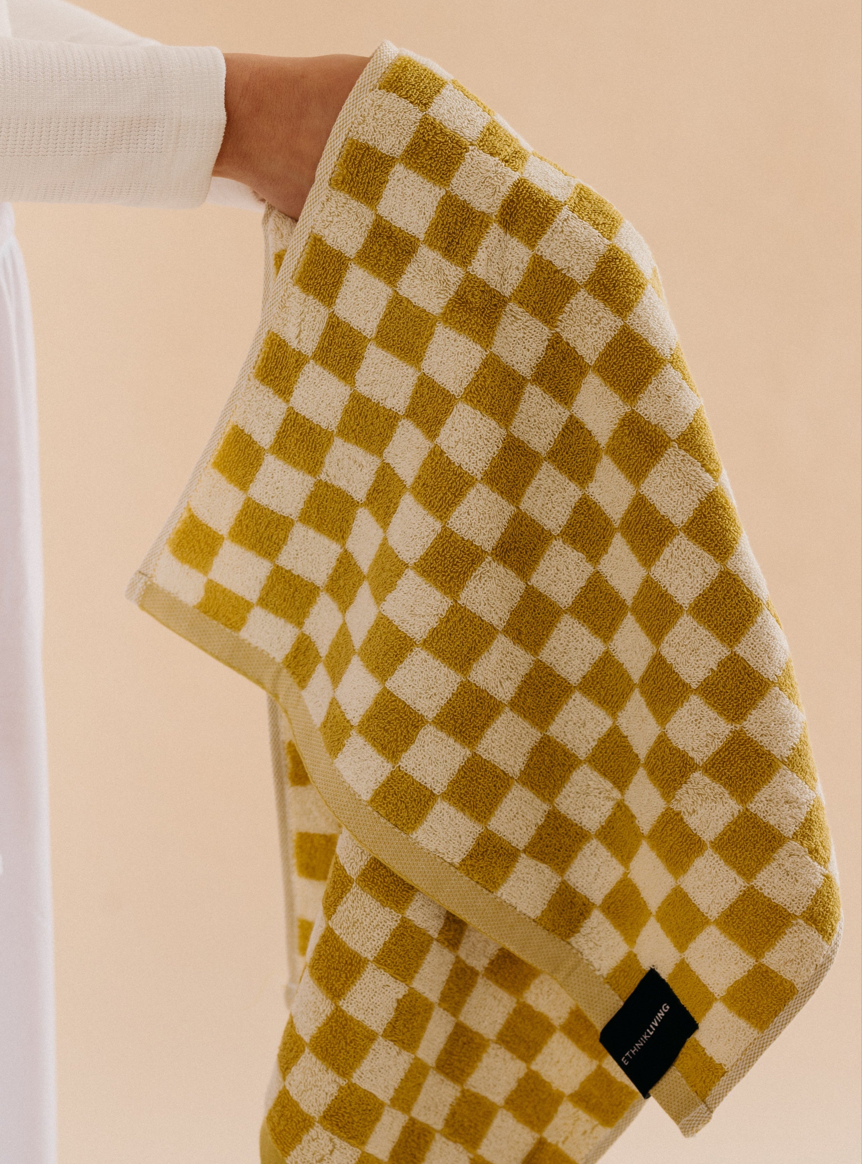 Hand holding a yellow and cream checkered cotton towel with a textured weave and a small Ethnik Living label, shown against a soft neutral background.