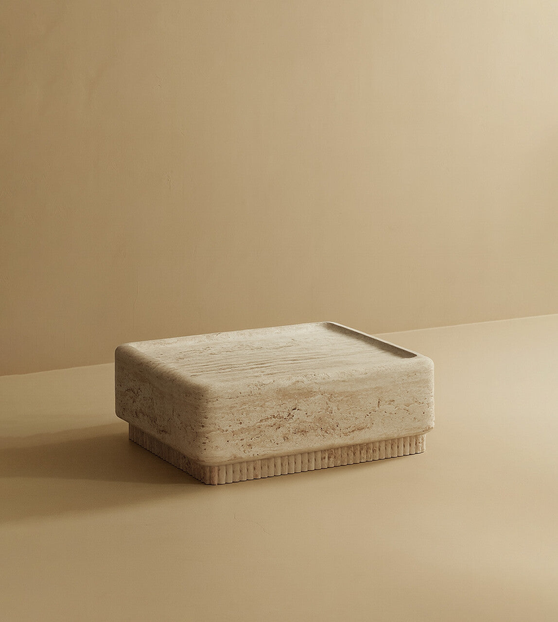 Square coffee table made from light travertine stone with natural tonal variation, featuring a solid block top and a low, ribbed base.