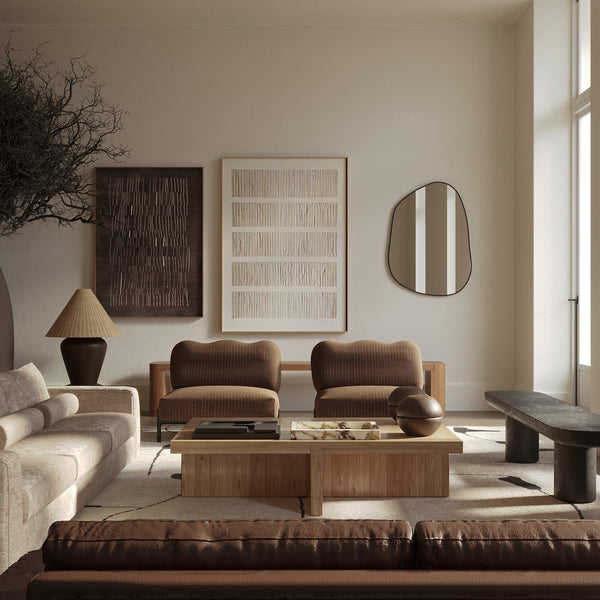 Neutral living room with a wooden coffee table, upholstered seating, abstract wall art, and an organic-shaped wall mirror reflecting a window.