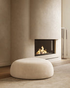 Pebble-style round white ottoman placed on a rug beside a fireplace.