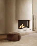 Pebble-style round brown ottoman placed on a rug beside a fireplace.