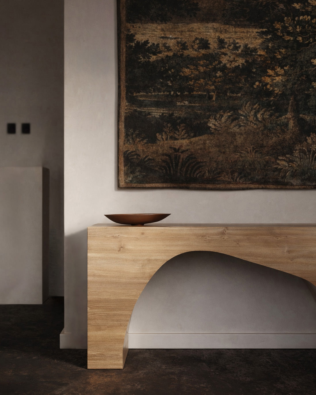 Wood console table with an arched base positioned against a wall beneath a large wall tapestry.