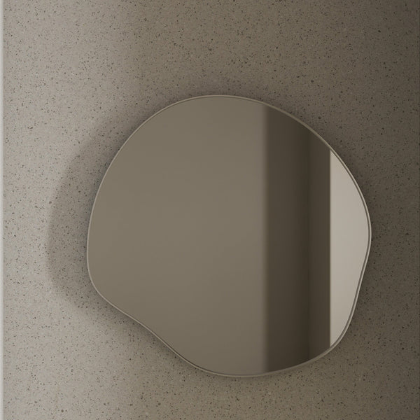 Organic-shaped wall mirror with a slim stainless steel frame mounted on a textured stone wall.