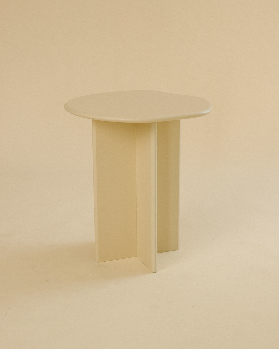 A minimalist side table featuring a round tabletop and three vertical legs in a light cream finish, photographed in a neutral studio setting.