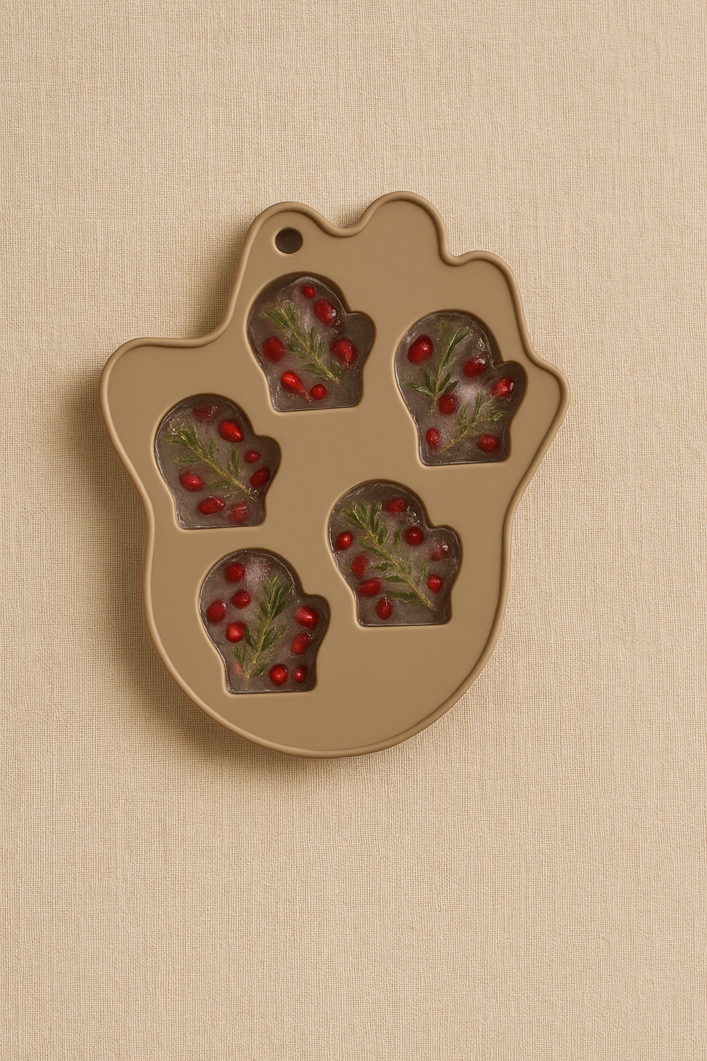 Mitten-shaped silicone mold with ice cubes containing pomegranate seeds and rosemary.