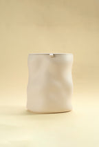 A beige sculptural dustbin with a fitted lid, photographed against a light yellow background.