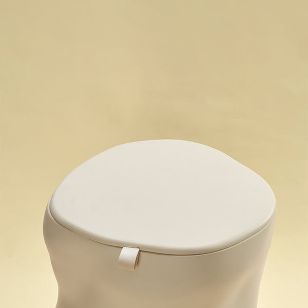 A beige sculptural dustbin with a fitted lid and a small front pull tab, photographed against a light yellow background.