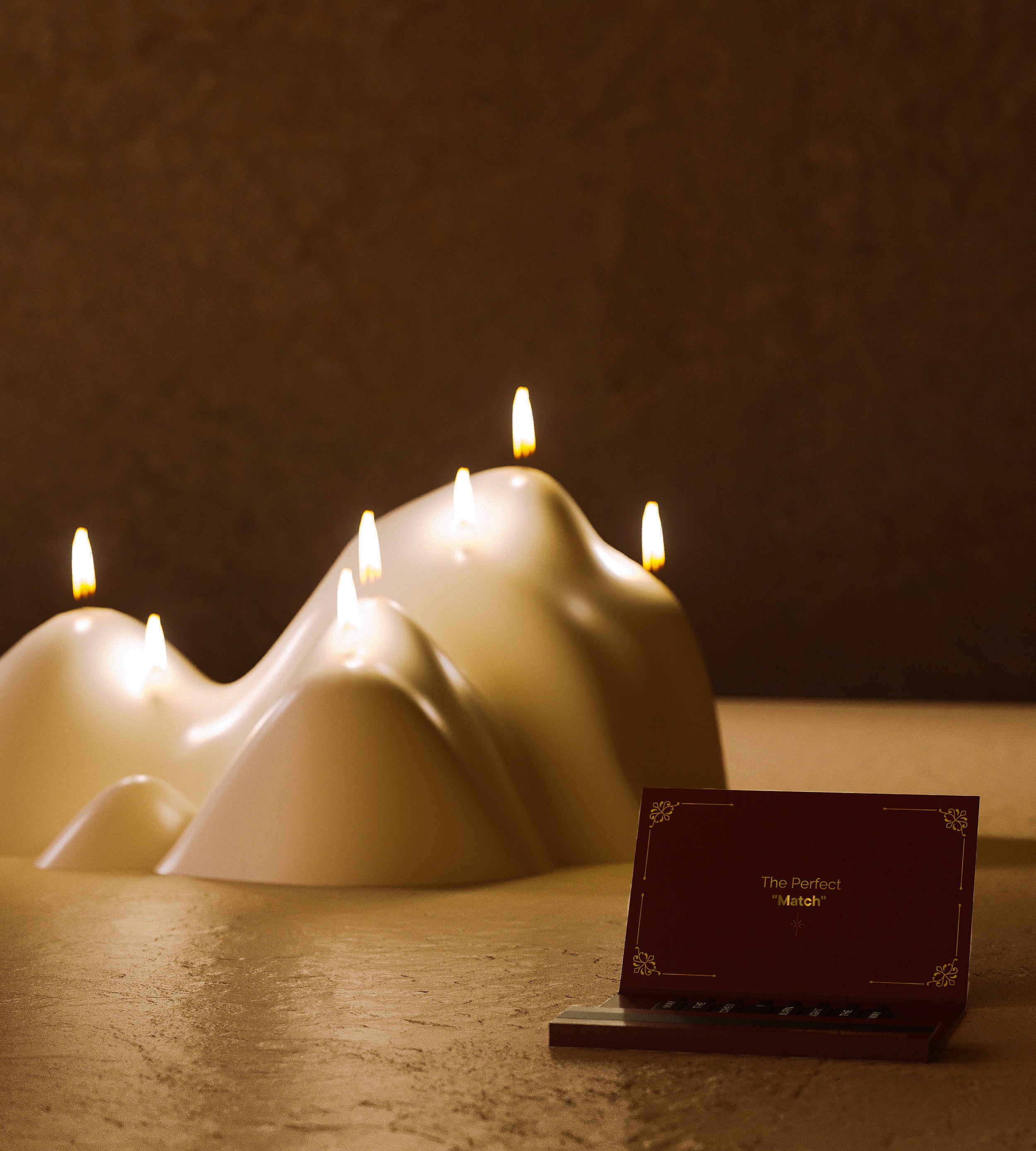 Mountain-shaped white candle with several lit wicks, styled next to an open matchbox in a warm, atmospheric setting.